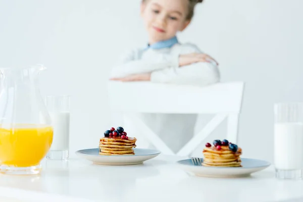 Selective focus of little kid looking at homemade pancakes with berries and honey on table — Stock Photo