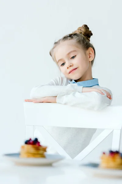 Маленька дитина дивиться на домашні млинці з ягодами та медом на столі — стокове фото