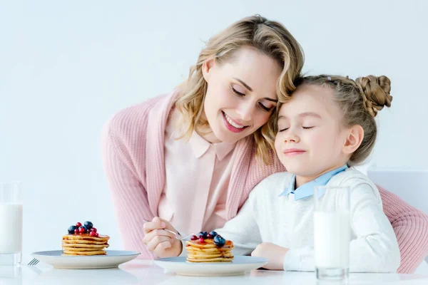 Mother hugging little daughter while having breakfast together at table — Stock Photo