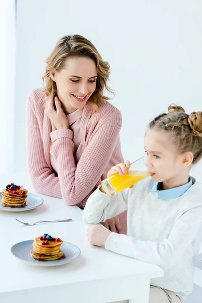 Sonrientes madre e hija desayunando juntas en la mesa - foto de stock