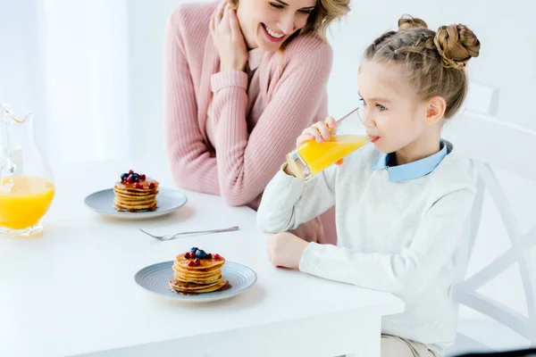 Улыбающиеся мать и дочь завтракают вместе за столом — стоковое фото