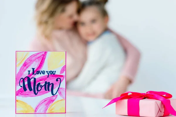 Selective focus of i love you mom postcard, wrapped gift and hugging family on background — Stock Photo