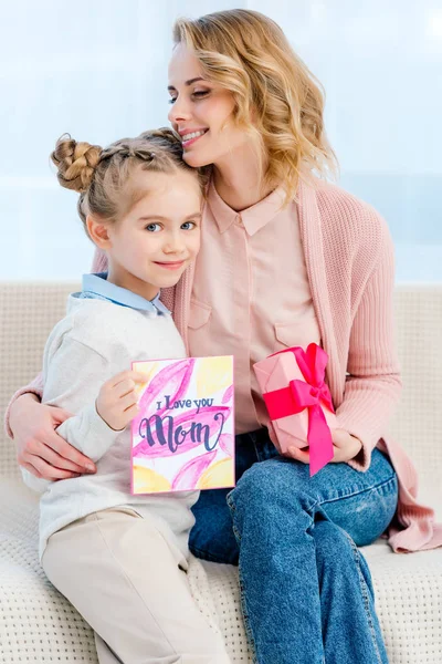 Mãe abraçando filha adorável e mostrando cartão postal no dia das mães felizes — Fotografia de Stock