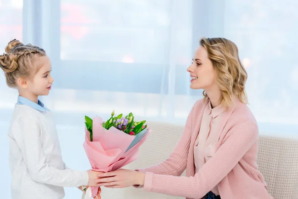 Vista lateral de la hija presentando ramo de flores a la madre en el día feliz de las madres - foto de stock