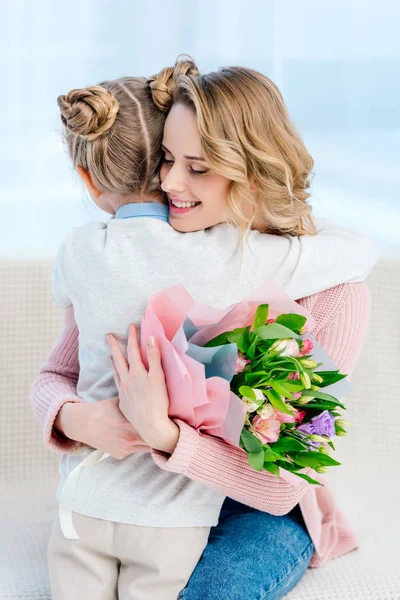 Mère heureuse embrassant fille et tenant bouquet sur la fête des mères heureuses — Photo de stock