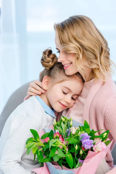 Mother hugging daughter and holding bouquet on happy mothers day — Stock Photo