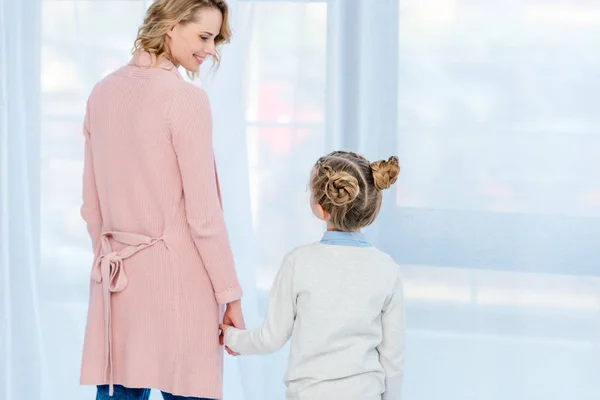 Vista posterior de la madre y la hija cogidas de la mano en casa - foto de stock