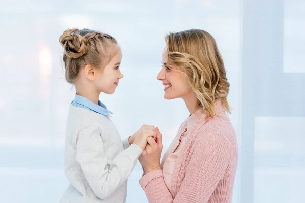 Vista lateral de mãe sorridente e filha de mãos dadas em casa — Fotografia de Stock