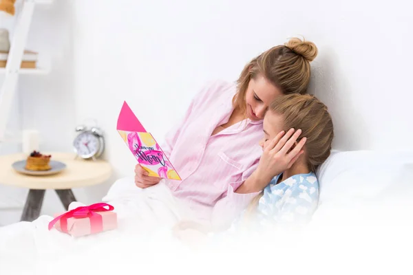 Mother hugging daughter and holding postcard on happy mothers day — Stock Photo