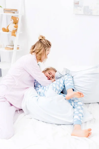 Мать щекочет дочь на кровати дома — стоковое фото