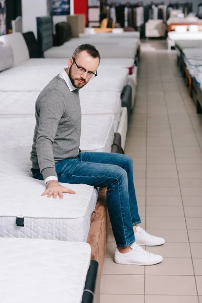 Side view of male customer in eyeglasses choosing mattress in furniture shop — Stock Photo