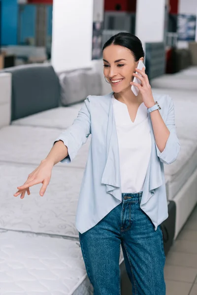 Smiling woman talking on smartphone while choosing mattress in furniture store — Stock Photo