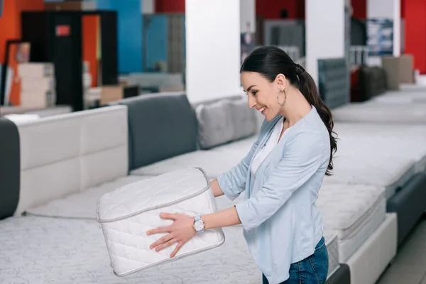 Femme souriante avec matelas pliant dans les mains dans le magasin de meubles — Photo de stock