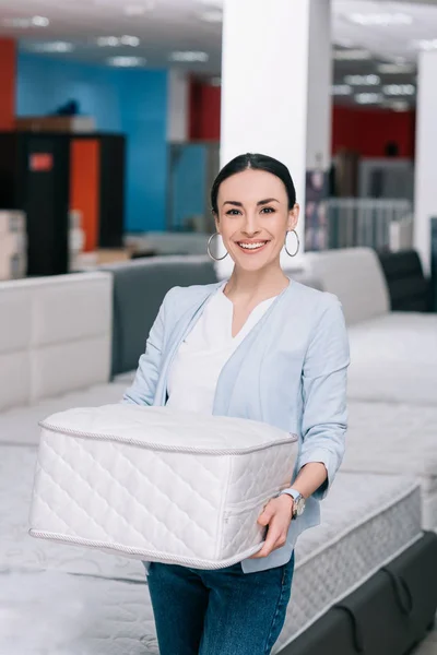 Femme souriante avec matelas pliant dans les mains dans le magasin de meubles — Photo de stock