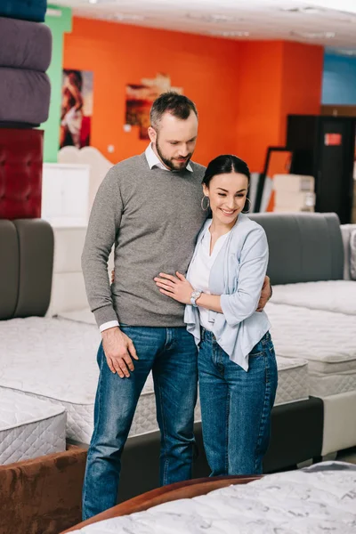 Pareja abrazando mientras que elige el colchón juntos en tienda de muebles - foto de stock