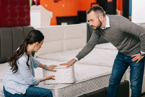 Couple choisissant matelas pliant ensemble dans le magasin de meubles avec matelas disposés — Photo de stock