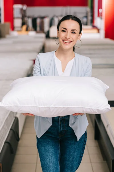 Портрет улыбающейся женщины, показывающей подушку в мебельном магазине — стоковое фото