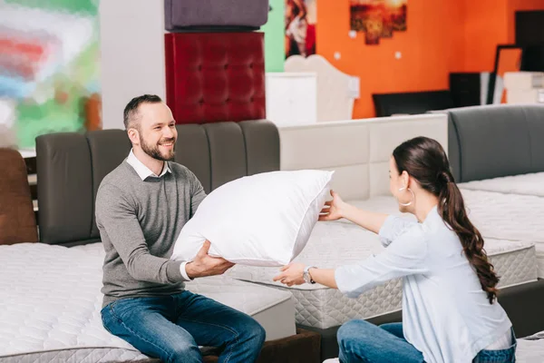 Couple souriant avec oreiller dans le magasin de meubles avec matelas disposés — Photo de stock