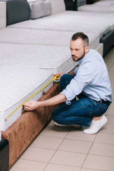 Male shopper measuring orthopedic mattress with measure tape in furniture store — Stock Photo