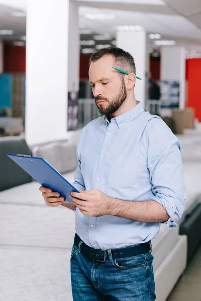 Portrait of focused shop assistant with notepad in furniture shop with arranged mattresses — Stock Photo