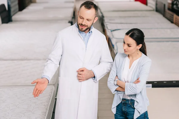 Assistente di negozio maschio in cappotto bianco che mostra le merci al cliente nel negozio di mobili — Foto stock