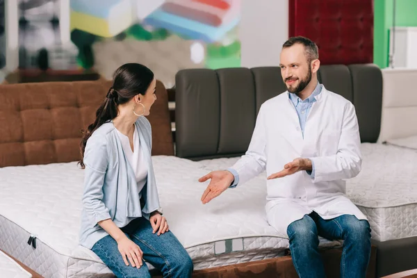 Male shop assistant in white coat showing goods to customer in furniture shop — Stock Photo