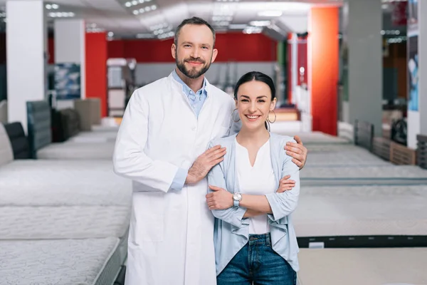 Portrait of smiling shop assistant and female shopper in furniture store with arranged mattresses — Stock Photo