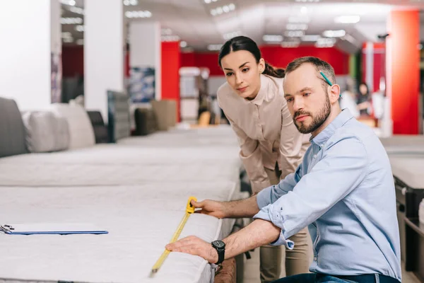 Couple measuring mattress with measure tape in furniture store with arranged mattresses — Stock Photo