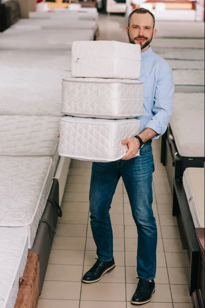 Чоловік тримає купу складних матраців в руках в магазині меблів — стокове фото