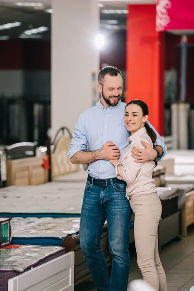 Happy couple in furniture store with arranged mattresses — Stock Photo