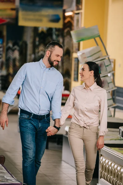 Smiling couple holding hands while walking in furniture store — Stock Photo