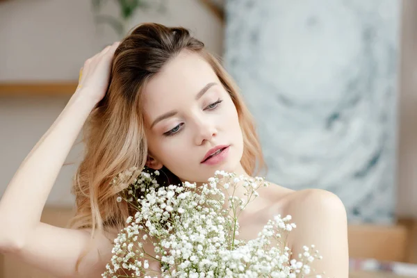 Retrato de bela menina nua sensual segurando flores brancas e olhando para longe no estúdio de arte — Fotografia de Stock