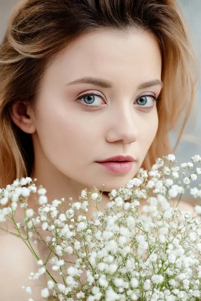 Retrato de cerca de la hermosa mujer joven con flores blancas y mirando a la cámara - foto de stock