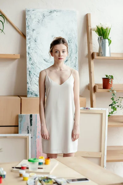 Hermosa mujer joven seria de pie en el estudio de arte y mirando a la cámara - foto de stock