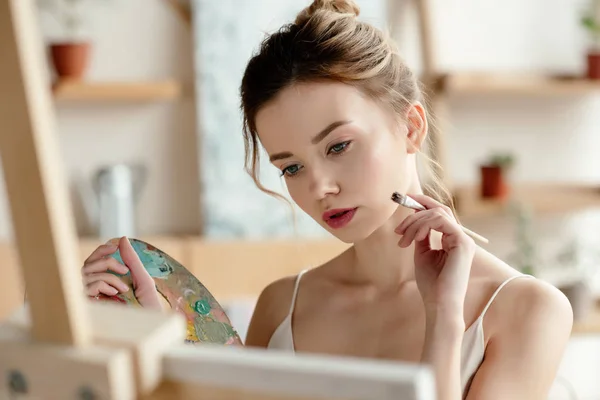 Menina atraente com pintura de pincel e paleta imagem no estúdio de arte — Fotografia de Stock