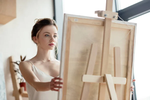Beautiful young artist looking at picture on easel — Stock Photo