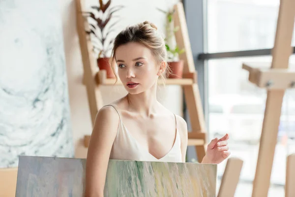 Beautiful pensive girl holding picture and looking away in art studio — Stock Photo
