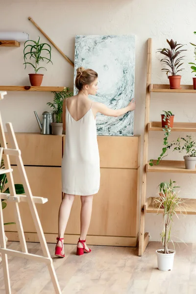 Rear view of tender young female artist holding picture in art studio — Stock Photo