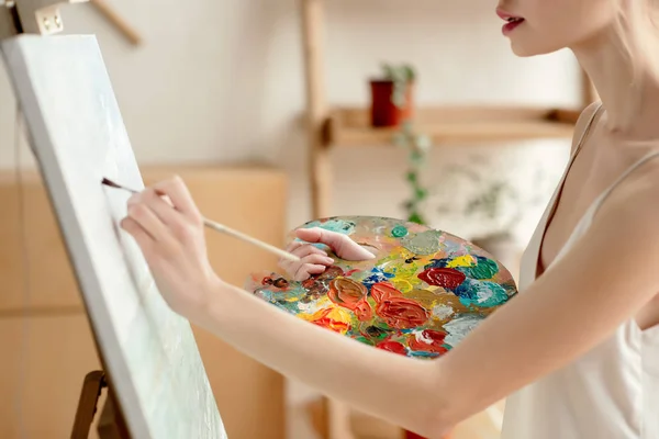 Cropped shot of tender young artist with palette and brush painting on easel in studio — Stock Photo
