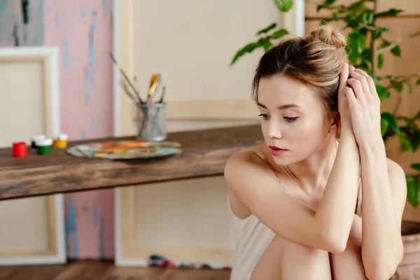 Beautiful pensive young woman sitting and looking away in art studio — Stock Photo