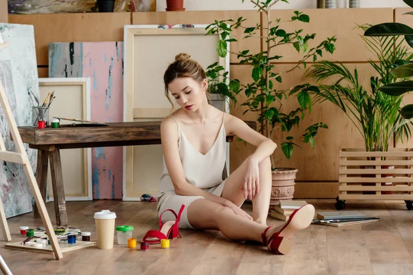 Frustrierte junge Künstlerin sitzt im Atelier auf dem Boden — Stockfoto