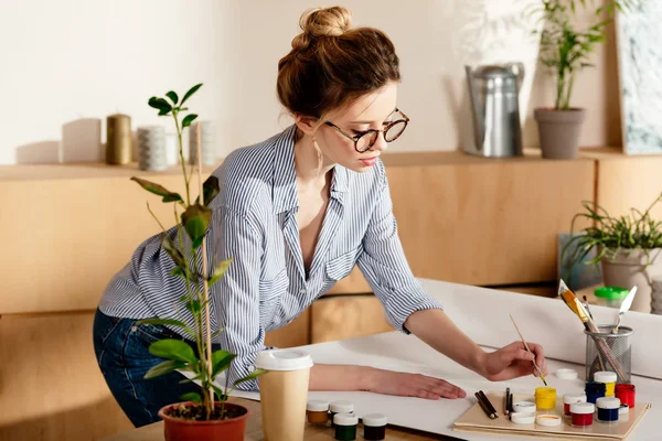 Beautiful young female artist drawing on table in studio — Stock Photo