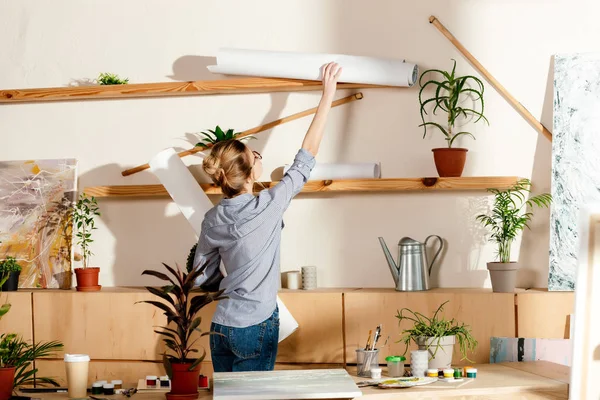 Vista trasera de la joven artista quitando lienzos de la estantería - foto de stock