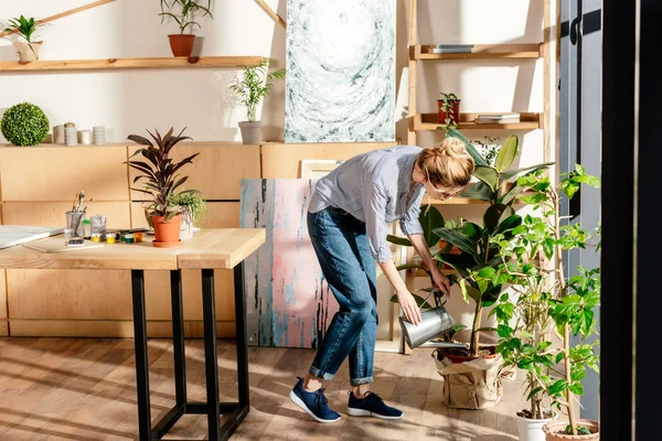 Élégant artiste féminine dans les lunettes arrosage pot plan en studio — Photo de stock