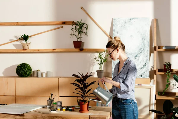 Side view of stylish woman in eyeglasses watering potted plan — Stock Photo