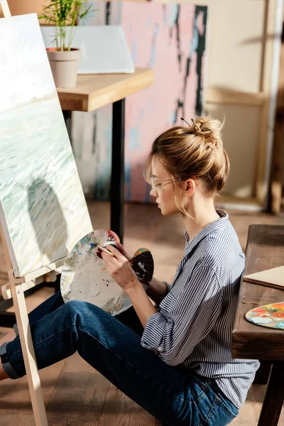 Vista lateral de artista feminina elegante em óculos pintura no cavalete — Fotografia de Stock