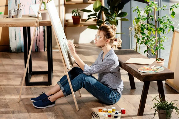 Jovem artista feminina elegante em óculos pintura no cavalete — Fotografia de Stock