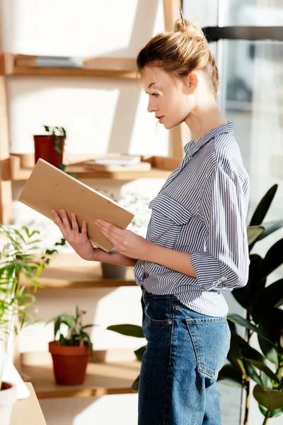 Side view of young woman reading book near potted plants — Stock Photo