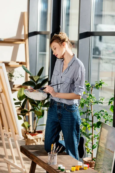 Artiste féminine parlant sur smartphone et peignant sur chevalet — Photo de stock