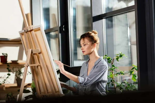 Young female artist painting on easel in art studio — Stock Photo